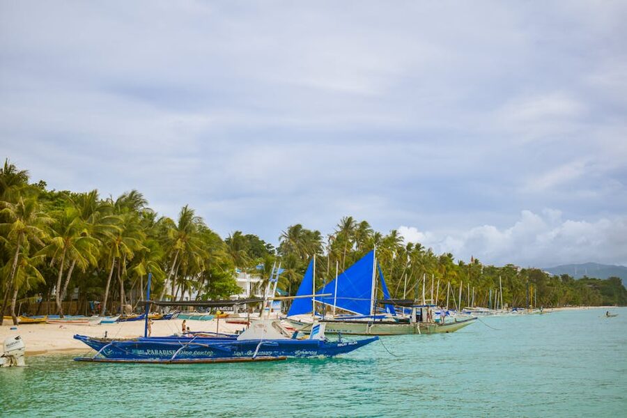 Boracay traditional paraw sailboats with blue sails on white sand beach