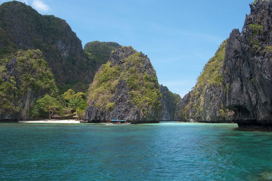 Limestone karst island in Bacuit Bay, El Nido, Palawan, with a single bangka boat on jade-green water