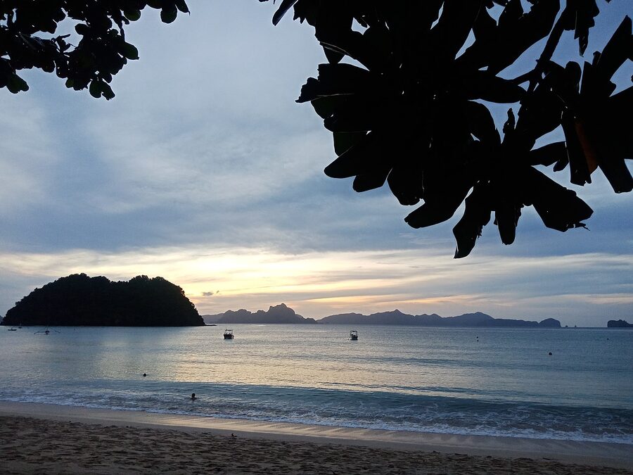 Sunset at El Nido, Palawan, with silhouetted islands and a bangka boat passing in front of a pink and orange sky