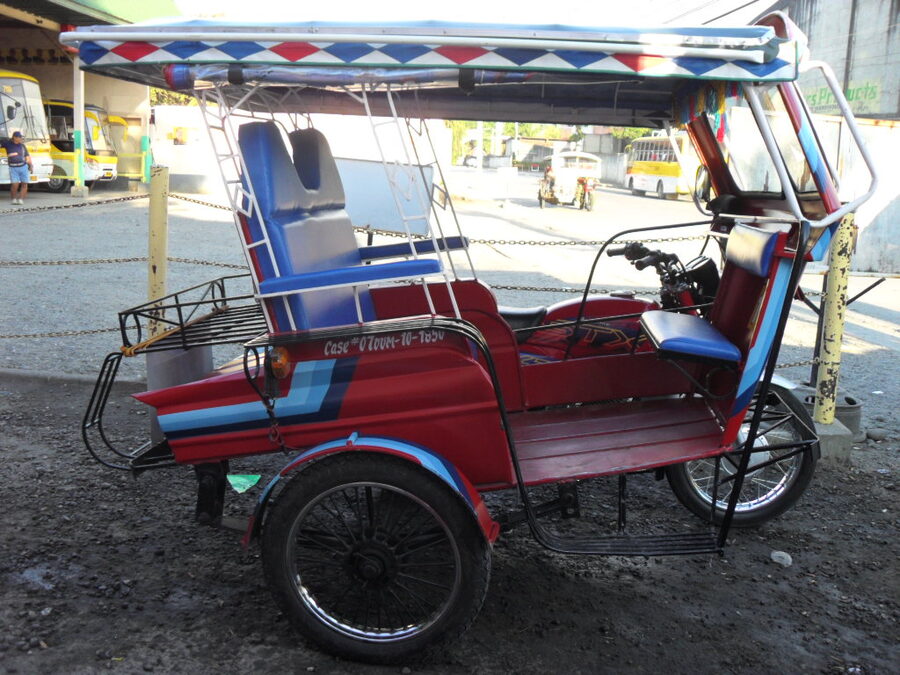 A traditional Philippine tricycle parked at a terminal with motorcycle and sidecar