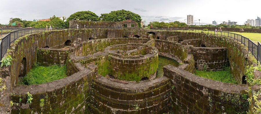 The circular ruins of the original Baluarte de San Diego with mossy stone walls and grass-covered chambers, Intramuros