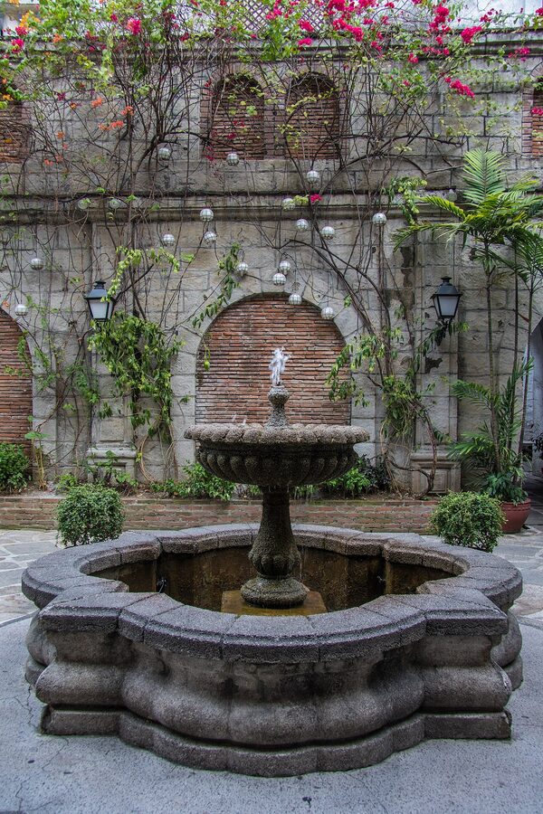 The interior courtyard fountain at Casa Manila, Intramuros, surrounded by red-brick walls and bougainvillea