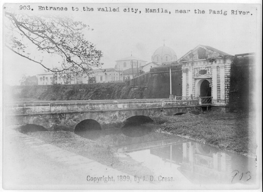 A 1899 photograph of the entrance to Intramuros, Manila, with the Puerta del Postigo gate, stone bridge, and city beyond