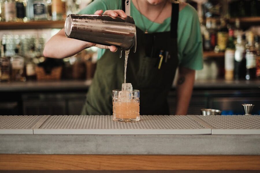 Bartender pouring a cocktail into a coupe glass at a dimly lit bar
