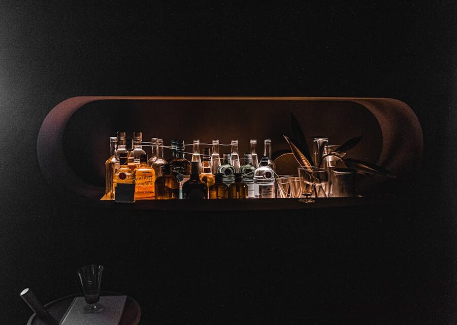 Backlit liquor bottles on dark wooden shelving in a low-lit bar