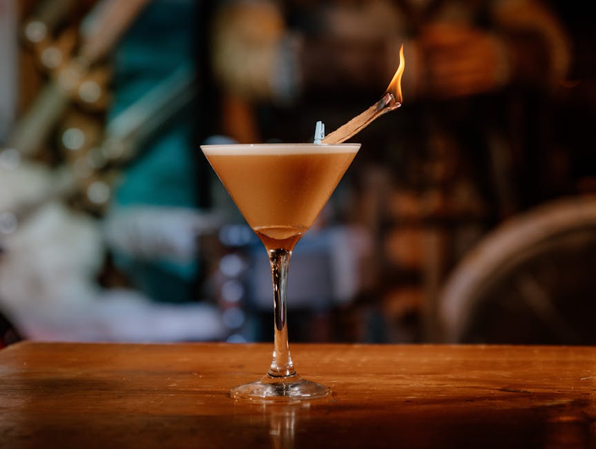 Cocktail in a martini glass with a flaming cinnamon garnish on a wooden bar top