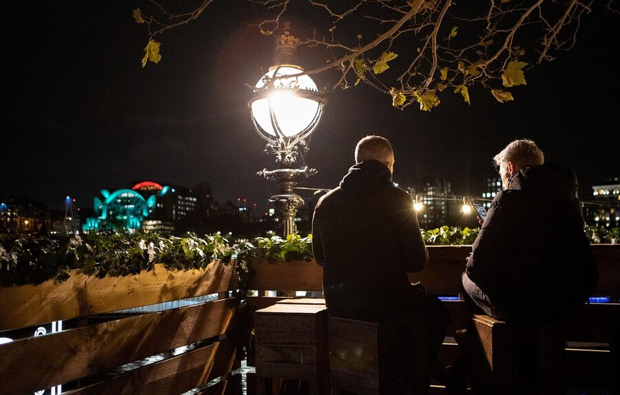 Group of friends drinking at a rooftop bar at dusk with city skyline behind