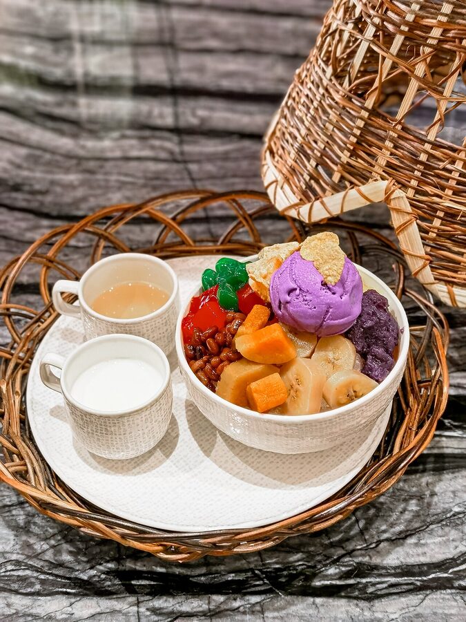 A serving of Filipino halo-halo in a coconut-shaped bowl with ube purple yam ice cream on top and jackfruit beans and sago