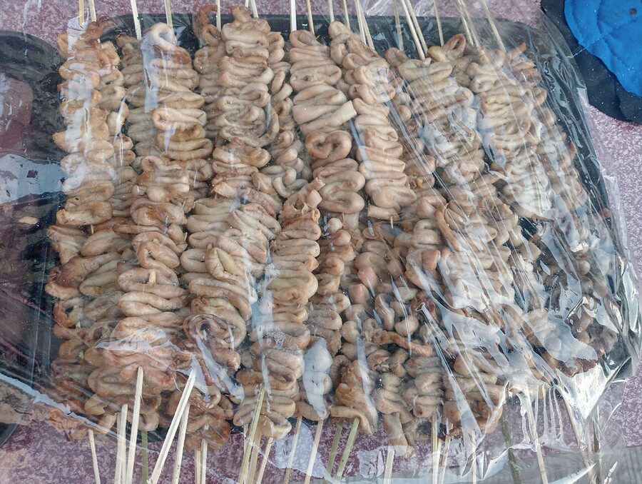 Trays of raw isaw skewers wrapped in plastic at a Manila street food stand ready for grilling