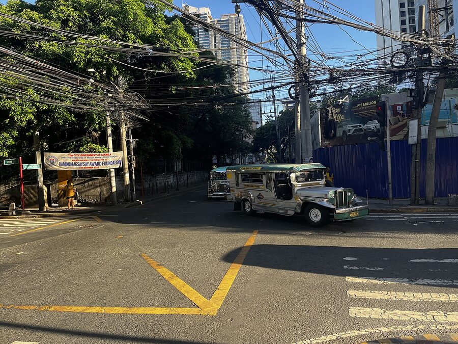 Manila side street with parked jeepneys overhead tangle of electrical wires and yellow road markings