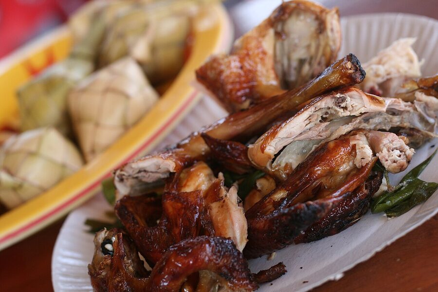 Filipino lechon manok rotisserie chicken pieces with crispy skin on a paper plate next to woven rice bundles