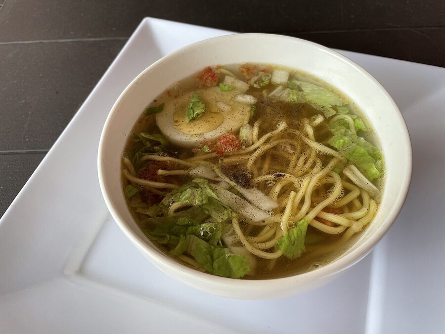 A bowl of Filipino-Chinese chicken mami noodle soup with sliced meat and green onion