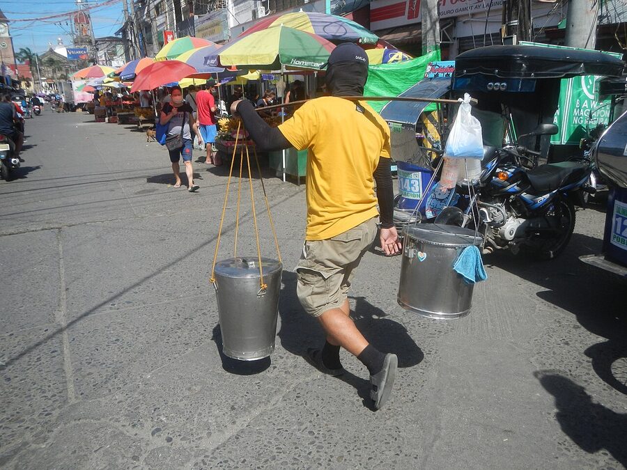 A Filipino taho vendor walking on a Manila street with a long pole carrying two metal buckets
