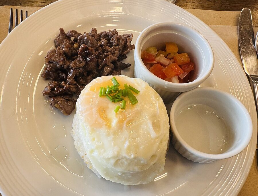 A plate of tapsilog with beef tapa garlic rice fried egg and a small bowl of pickled vegetables