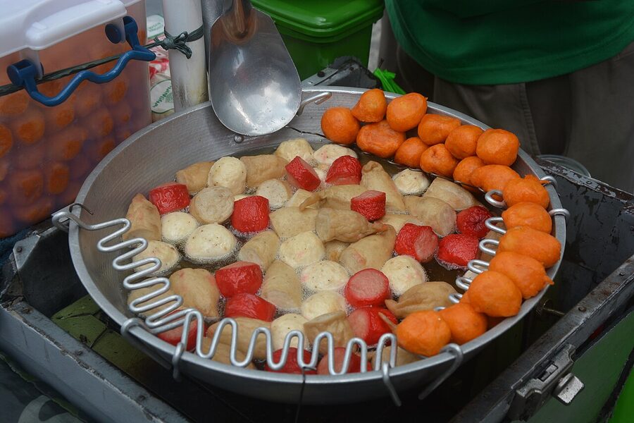 Pot of bobbing fishballs and bright orange kwek-kwek at a Manila street cart with a metal scoop