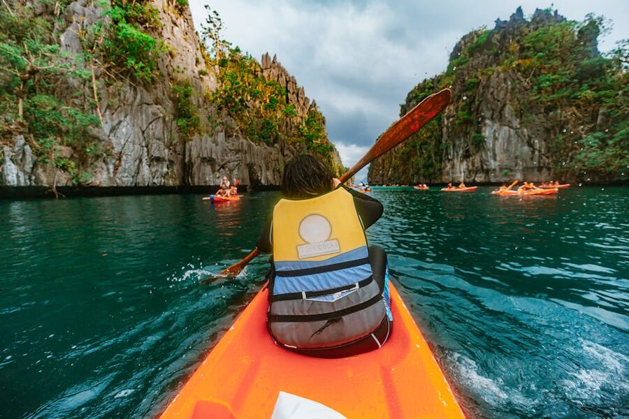Kayakers paddling through a turquoise lagoon ringed by limestone cliffs in El Nido Palawan