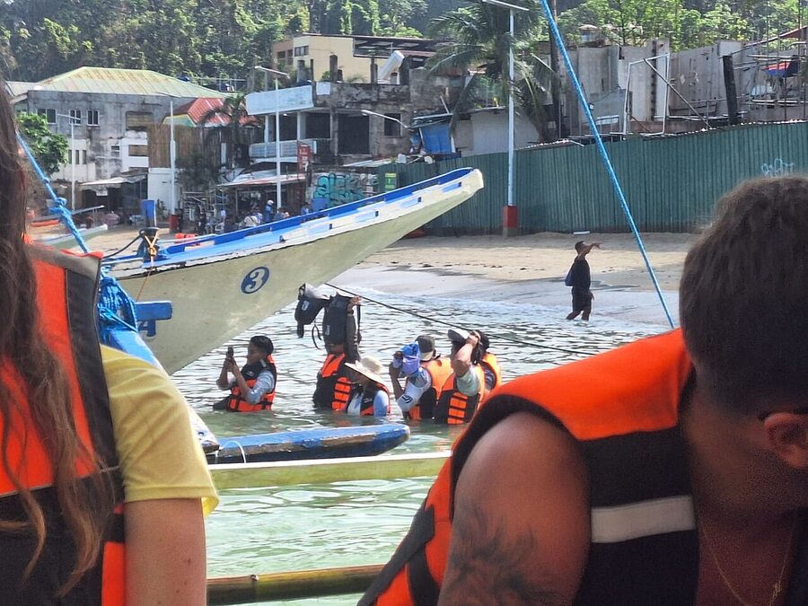 Tourists in life jackets boarding a bangka outrigger boat on a beach in El Nido for an island-hopping tour
