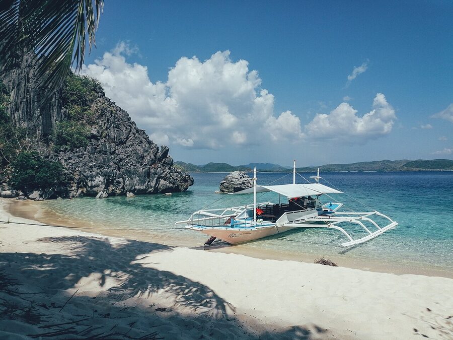 A bangka boat on a white sand beach with limestone cliff at Black Island, Coron, Palawan