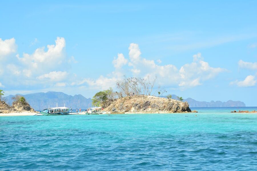A small island with a thin sandbar and tropical boats moored in turquoise water near Bulog Dos, Coron