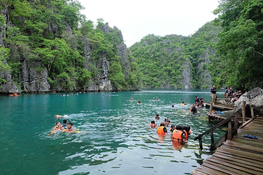 Swimmers and a wooden pier at Kayangan Lake, surrounded by limestone cliffs in Coron, Palawan