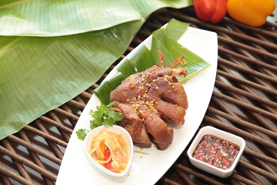 Crispy pata Filipino fried pork dish on a banana leaf with vinegar dipping sauce and chillies
